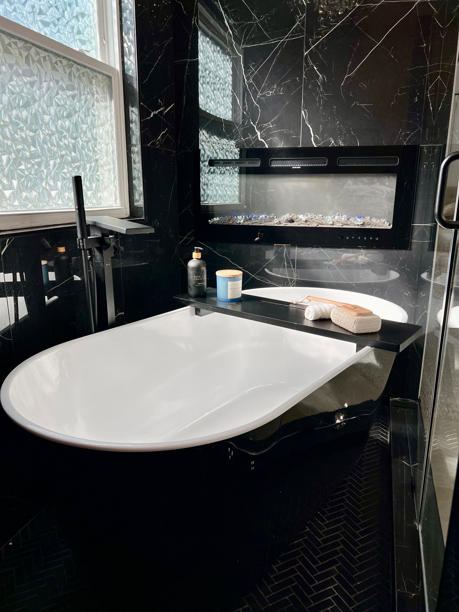 Freestanding white soaking tub set against black marble-look wall tiling