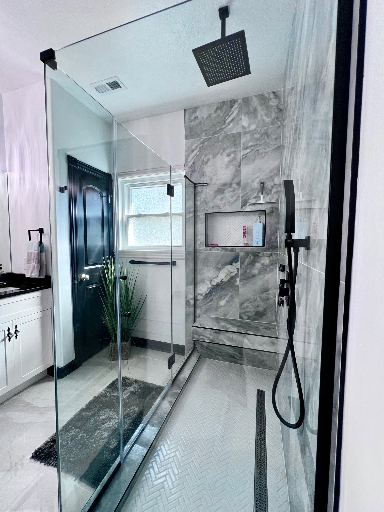 Modern walk-in shower featuring a glass enclosure with matte black hardware, herringbone tile flooring, large format wall tile, a built-in shower niche with mosaic tile, and a matte black rain shower head