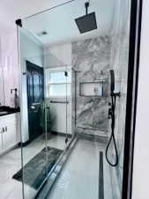 Modern walk-in shower featuring a glass enclosure with matte black hardware, herringbone tile flooring, large format wall tile, a built-in shower niche with mosaic tile, and a matte black rain shower head