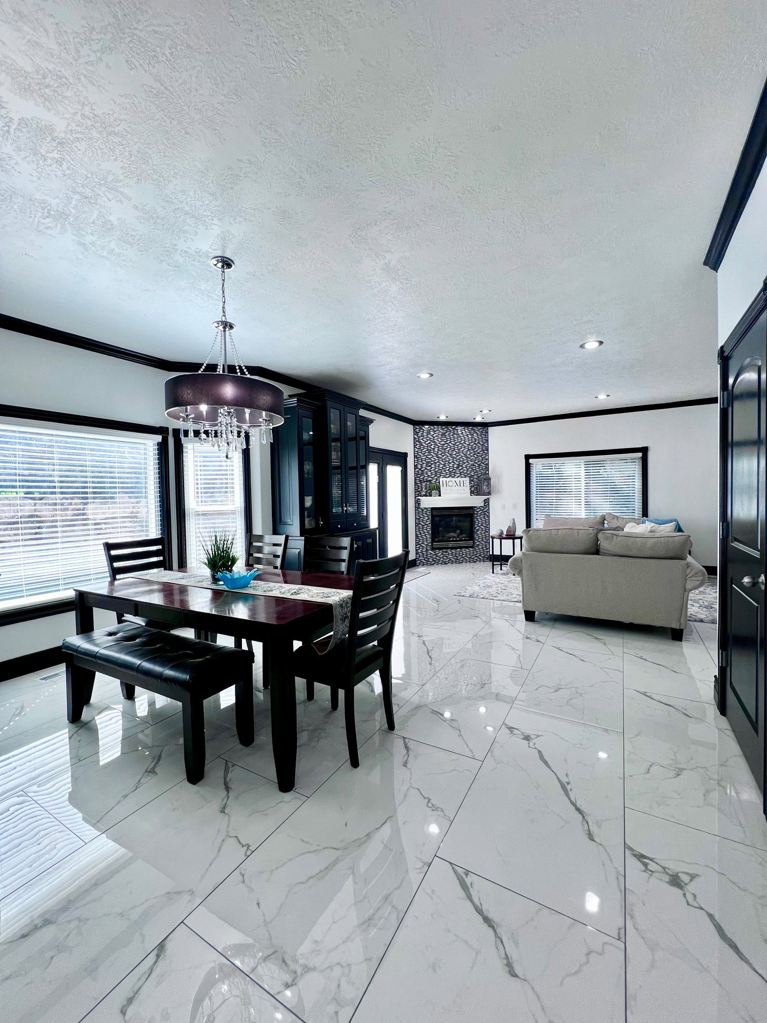 Spacious open-concept interior featuring large format marble-look tile flooring, a built-in fireplace with a mosaic tile surround, and recessed lighting