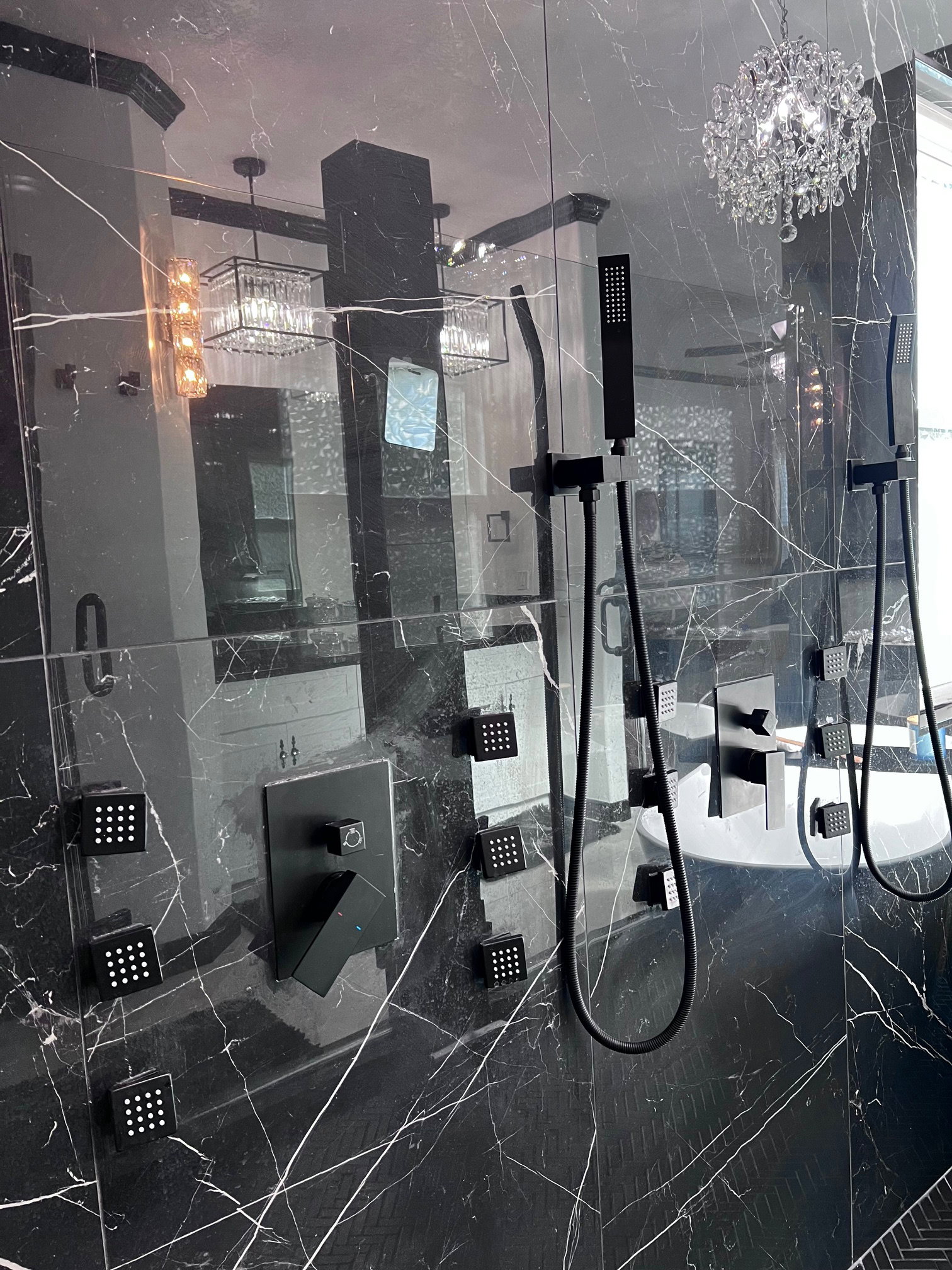 Spacious shower enclosure with black marble-finish wall paneling, a multi-function matte black shower system, and square body jets