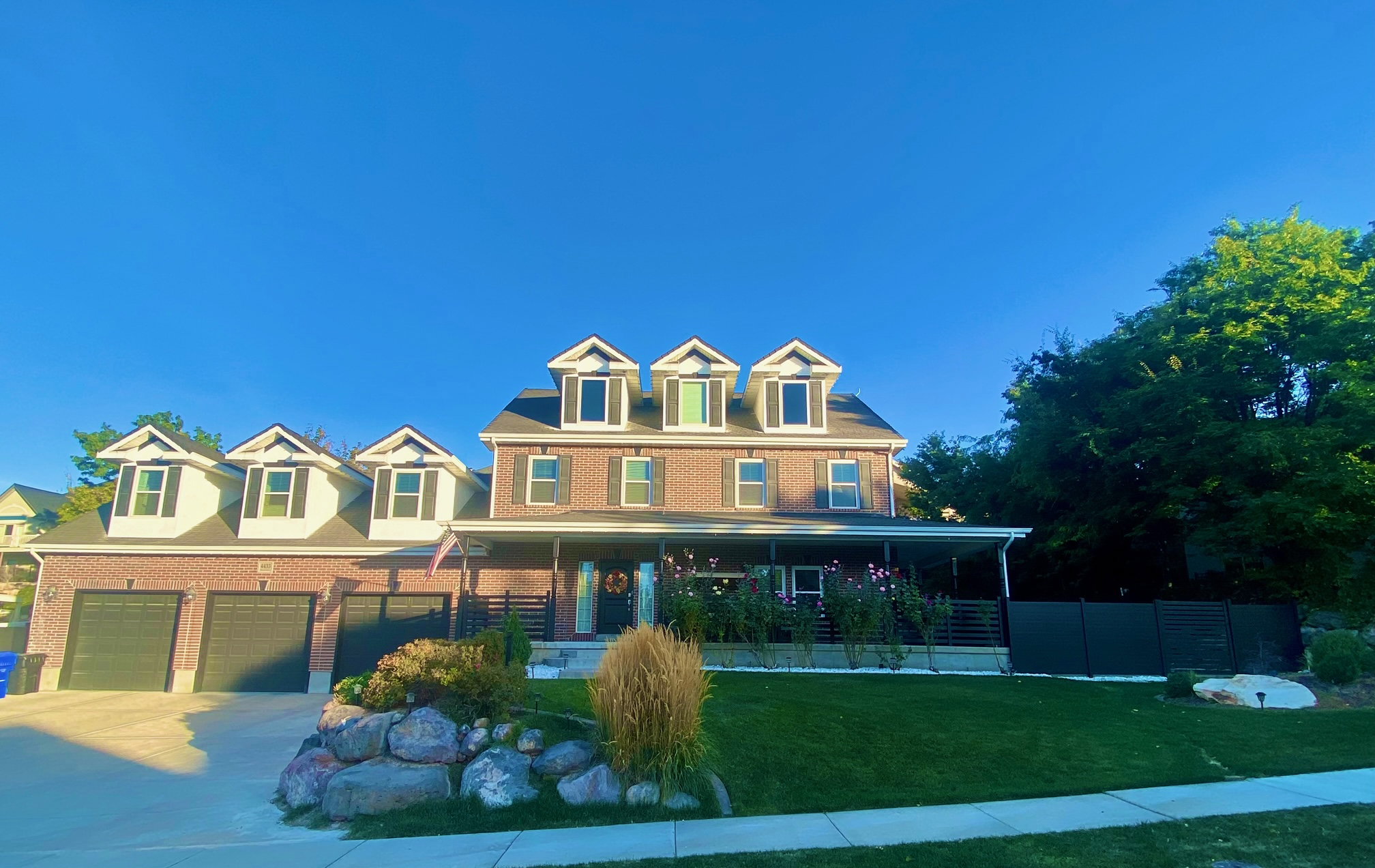 Brick facade residence featuring multiple dormer windows, a covered front porch, and an attached three-car garage