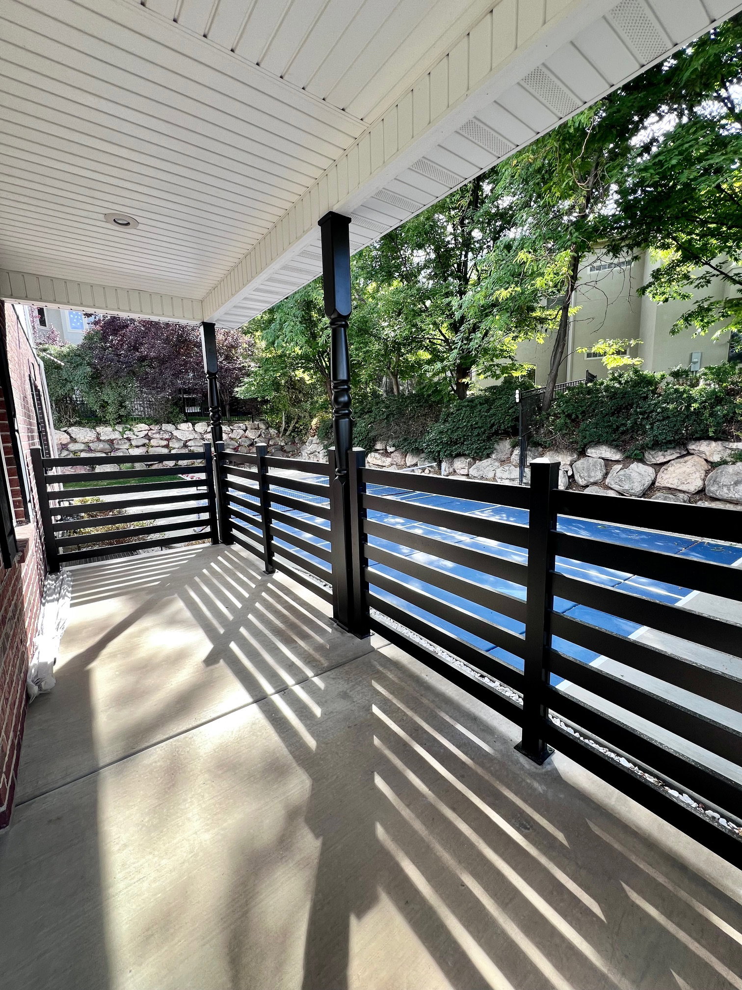 Covered porch featuring a slatted white soffit ceiling, brick exterior wall, and black horizontal slat railings