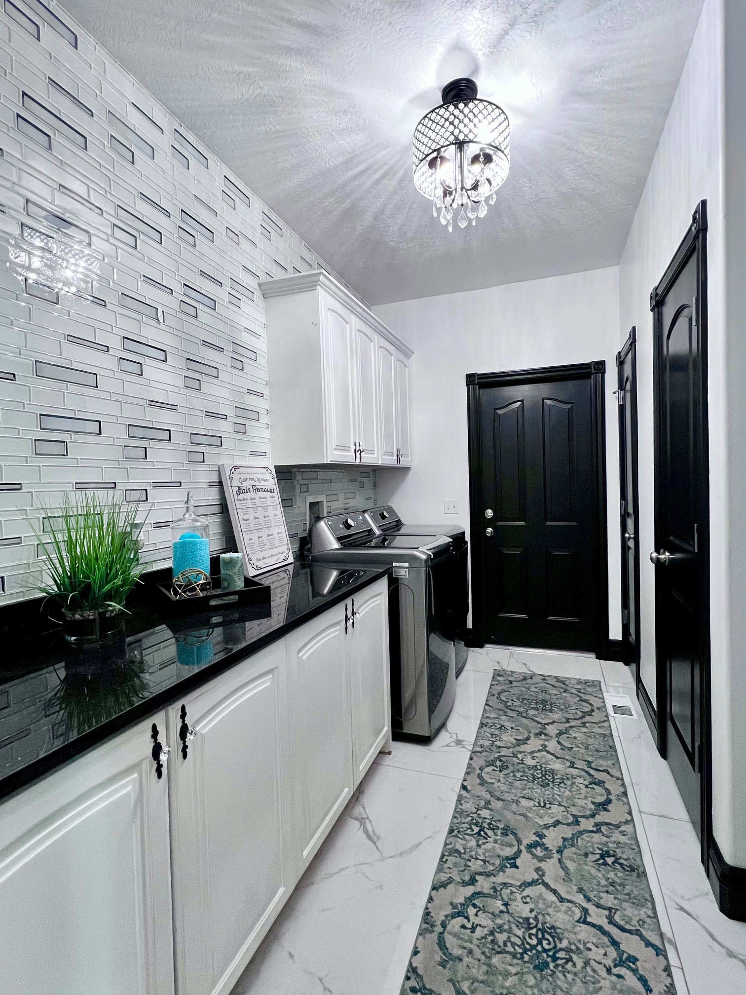 Laundry area featuring a stylish tile accent wall, white cabinetry with black hardware, black countertops, and polished tile flooring