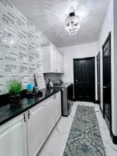 Laundry area featuring a stylish tile accent wall, white cabinetry with black hardware, black countertops, and polished tile flooring