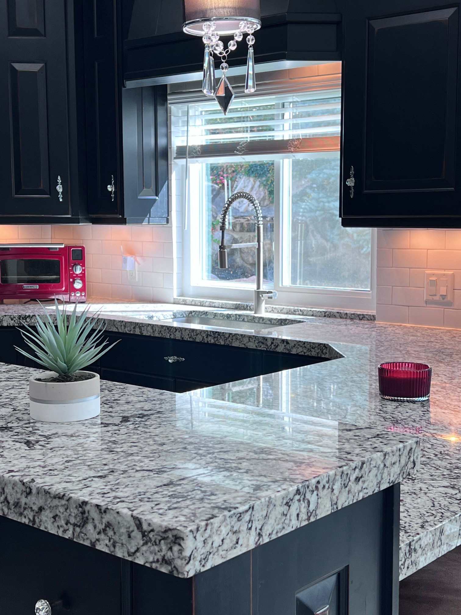 Kitchen featuring dark cabinetry, speckled countertops, undermount sink with gooseneck faucet, and subway tile backsplash