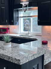 Kitchen featuring dark cabinetry, speckled countertops, undermount sink with gooseneck faucet, and subway tile backsplash