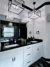 Dual crystal chandeliers illuminate a vanity featuring a black countertop, two undermount sinks, and white cabinetry with varied hardware