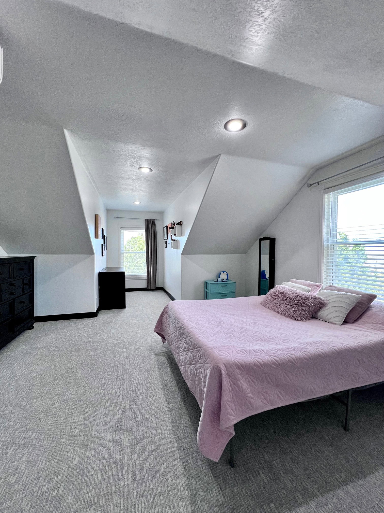 Vaulted ceilings with recessed lighting, light-toned carpeting, and a window with blinds providing natural light