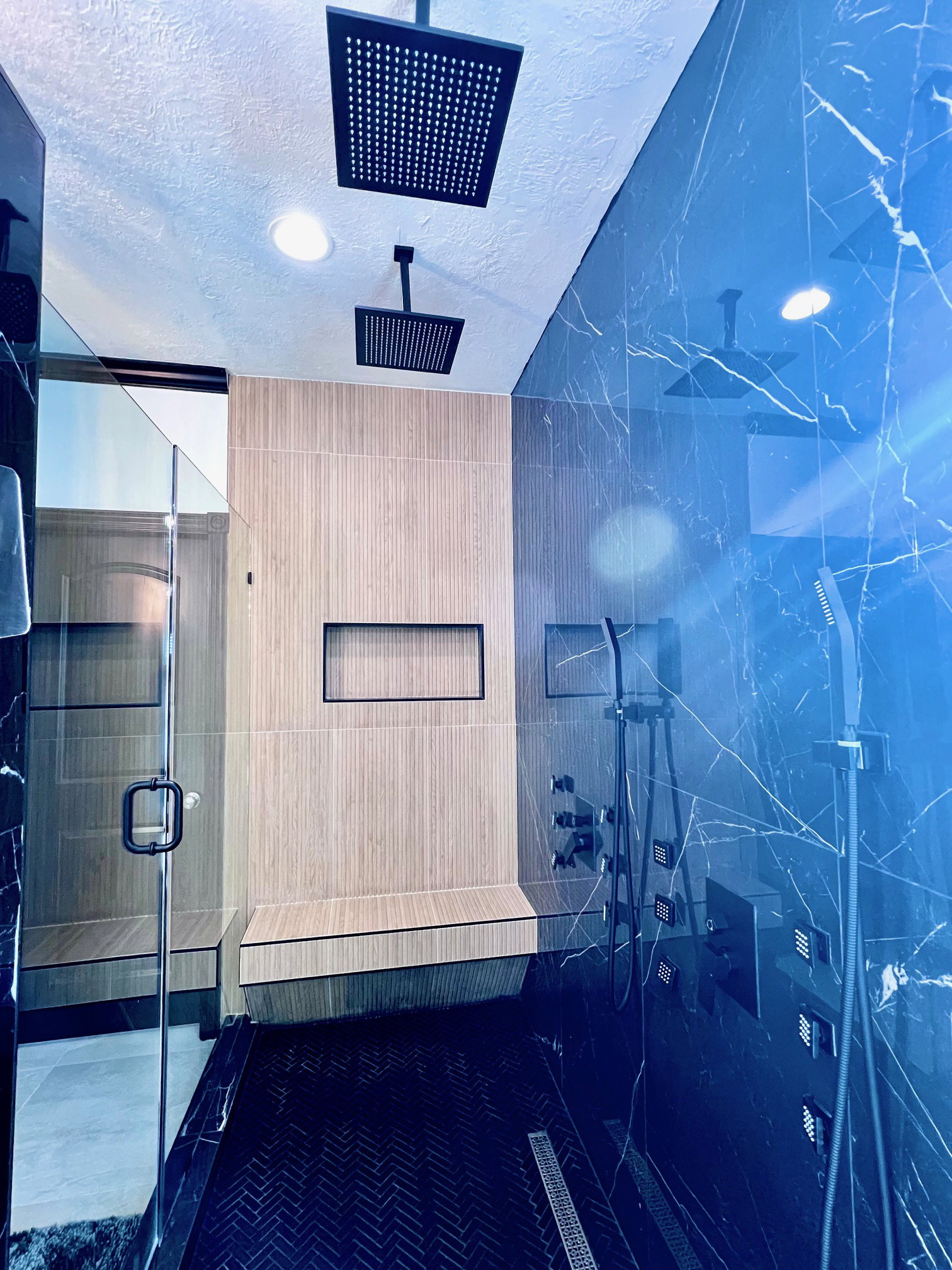 Walk-in shower featuring black marble-patterned wall panels, wood-finish wall tile, and a herringbone-patterned black shower floor