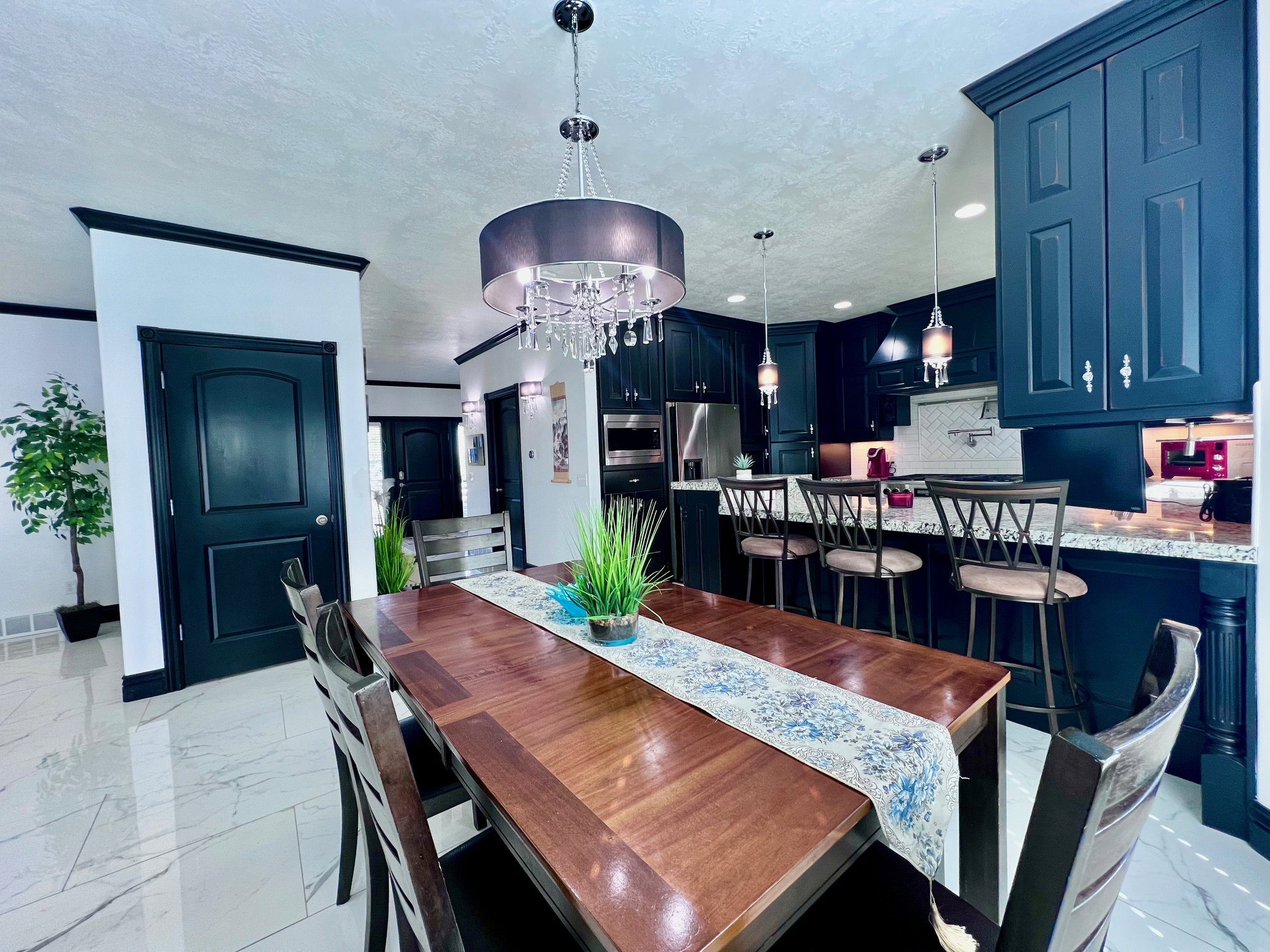 Open-concept dining area featuring a dark wood dining table, white tile flooring, and a contemporary chandelier