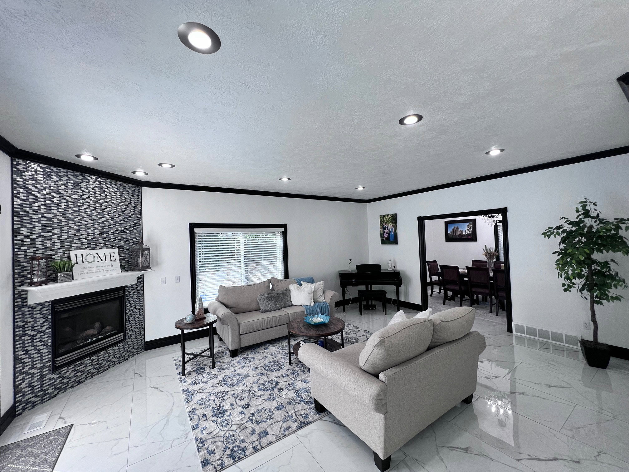 Spacious living area featuring large format white tile flooring, recessed ceiling lighting, and a fireplace with a mosaic tile surround and white mantel