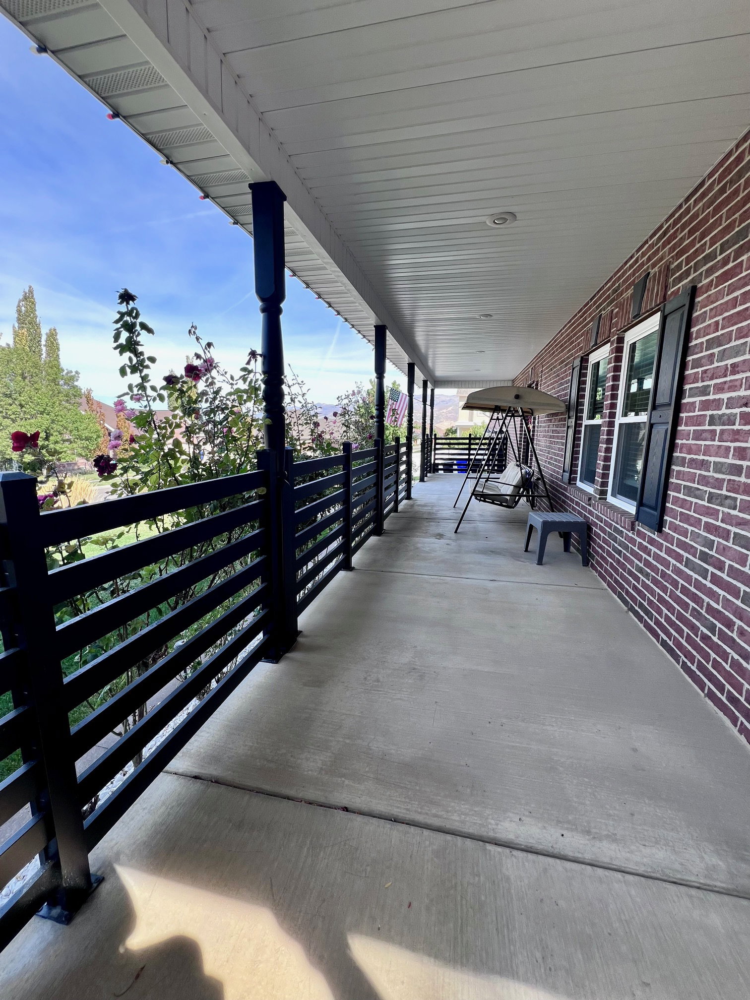 Expansive covered porch featuring a concrete surface, black horizontal railing, dark brick exterior, and recessed lighting
