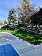 Manicured lawn area featuring a stone retaining wall, mature trees, and landscaping