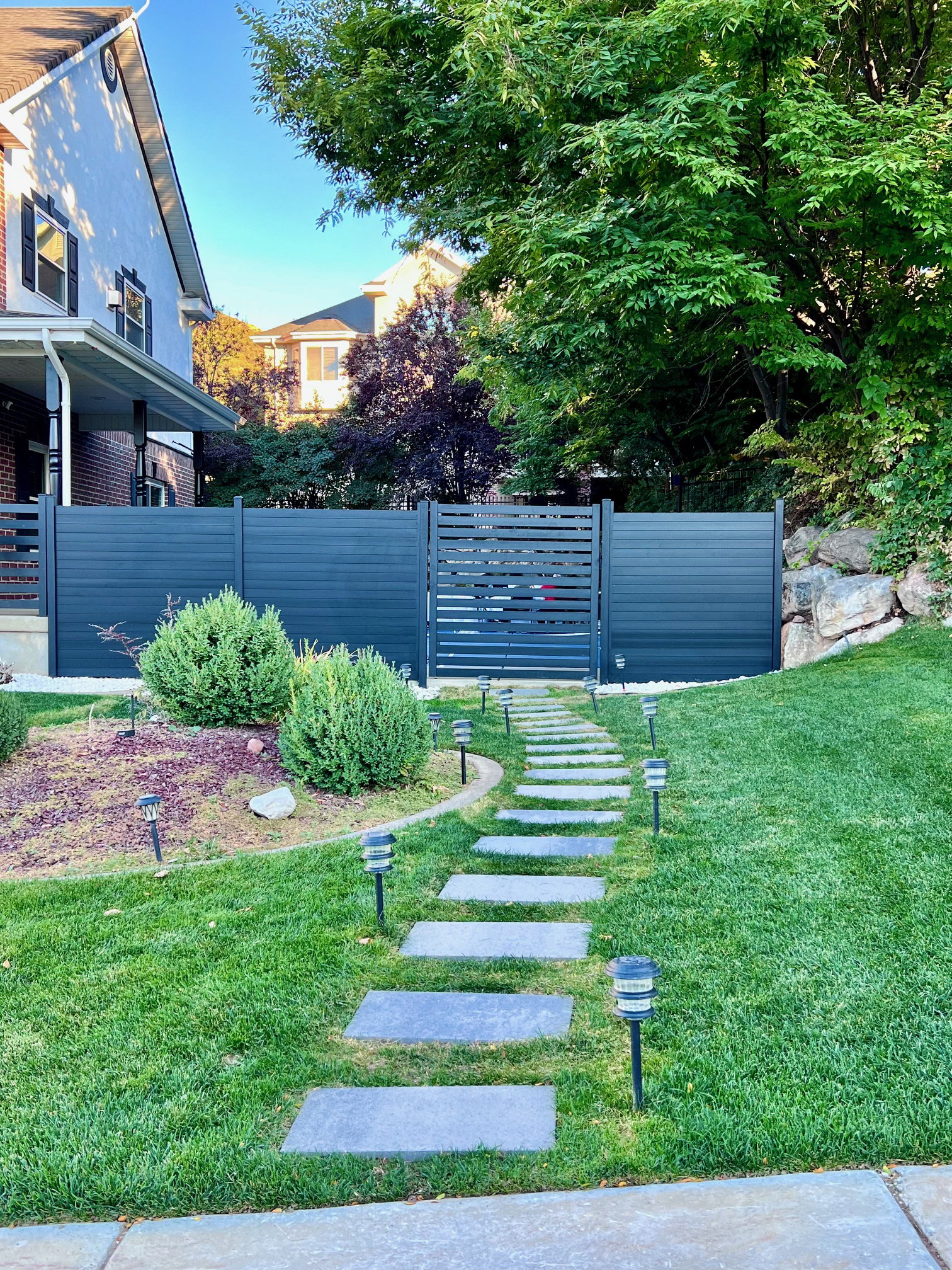 Modern privacy fence with integrated gate, bordered by a stone paver walkway and a manicured lawn