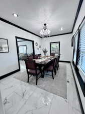 Dining area featuring white marble-look tile flooring, black crown molding, and a crystal chandelier