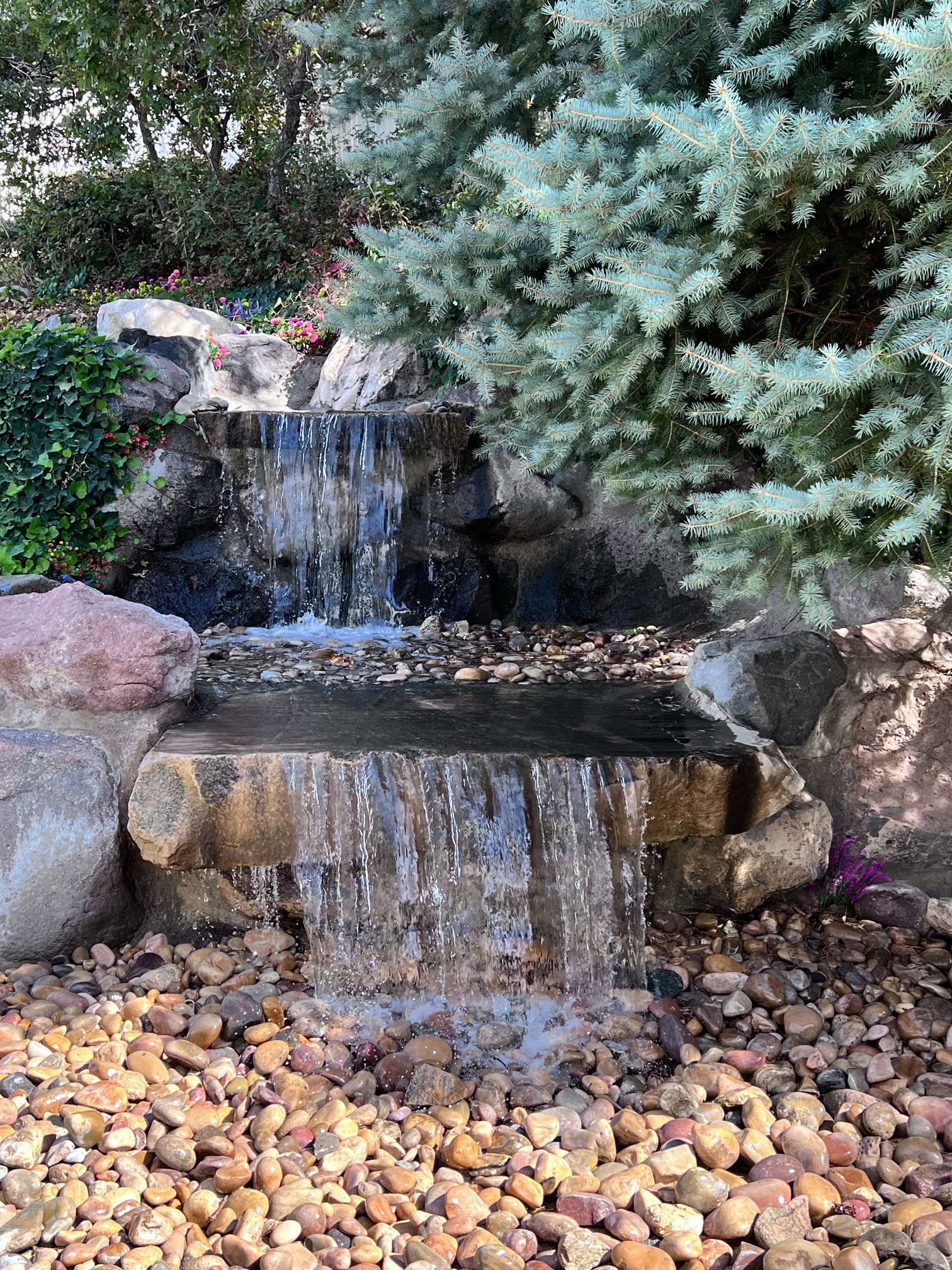 Tiered rock waterfall feature surrounded by river stones