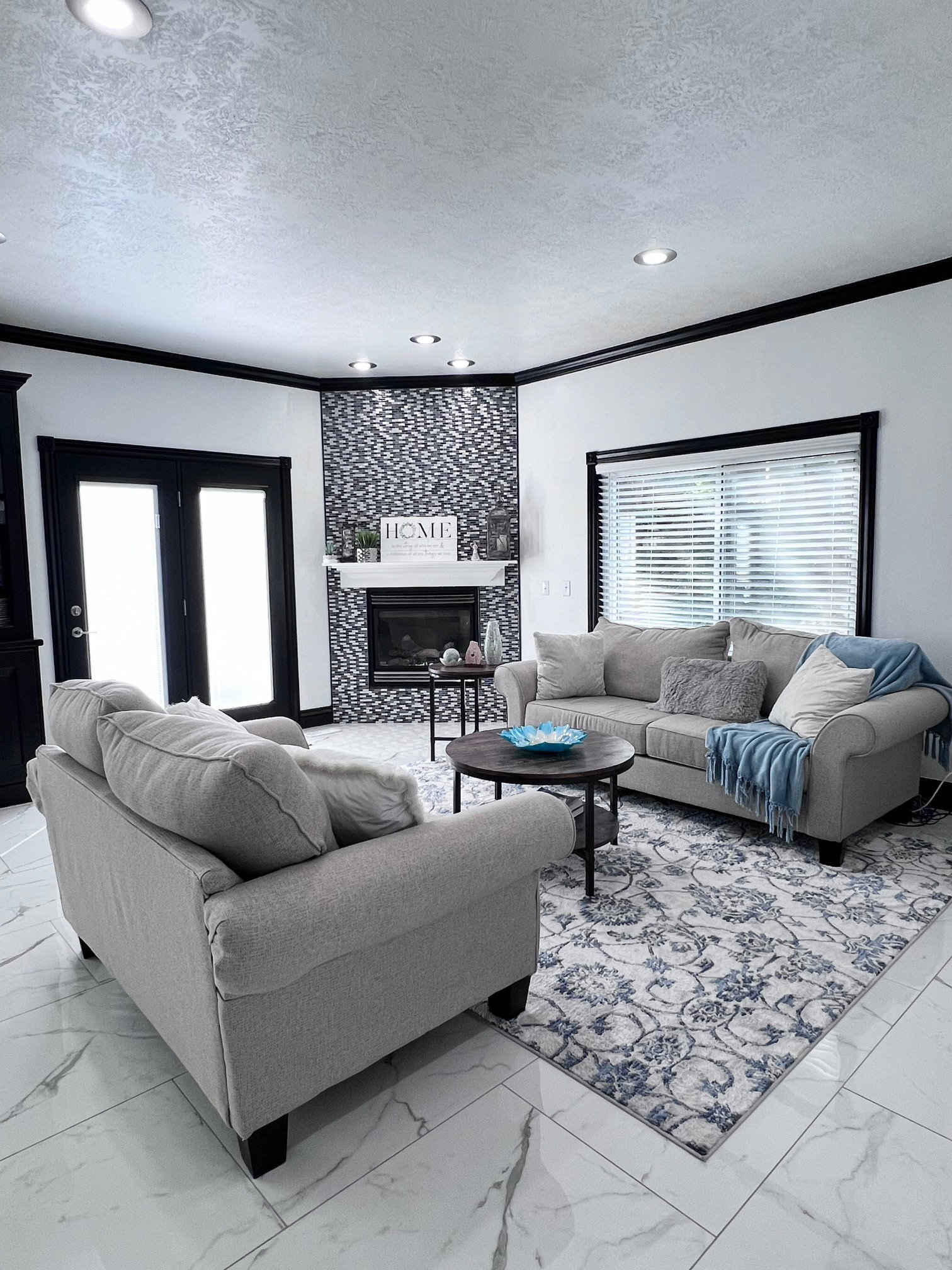 Spacious living area featuring polished marble-finish tile flooring, recessed lighting, and a corner fireplace with a decorative tile surround
