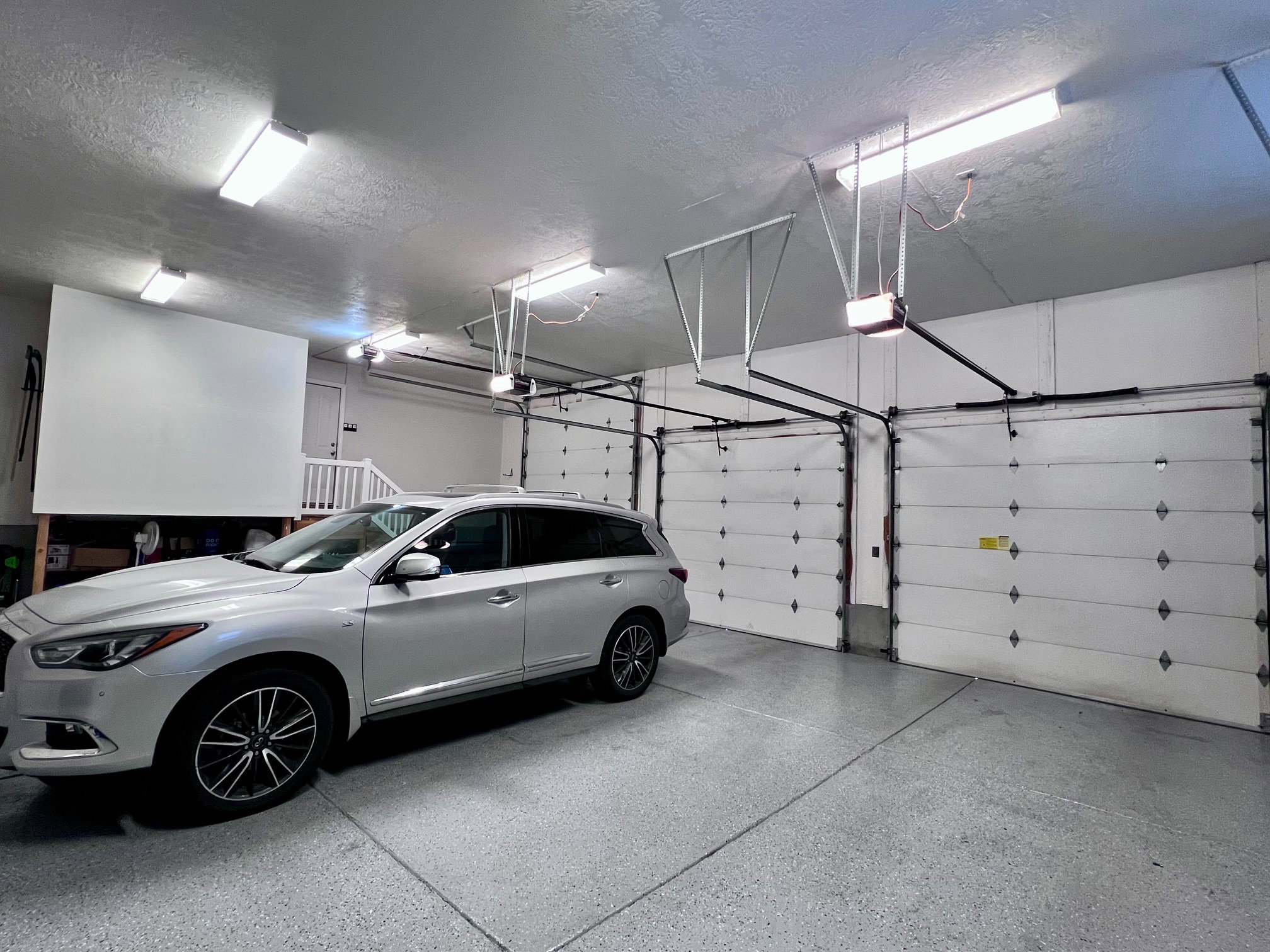 Spacious garage featuring two overhead doors with automatic openers, a durable epoxy-coated concrete floor, and multiple fluorescent ceiling light fixtures