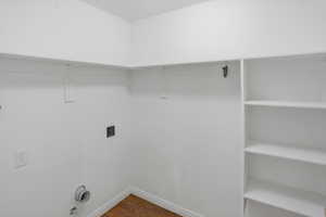 Dedicated utility space featuring built-in shelving, a clothes hanging rod, and wood-finish flooring. Electric and Gas dryer hookups