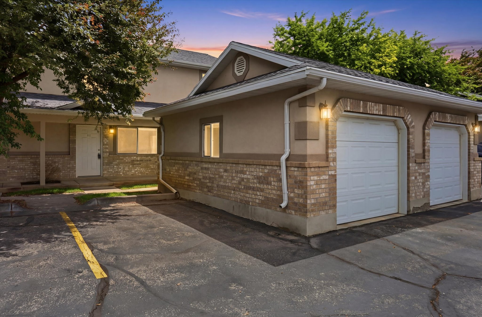 Exterior featuring a two-car garage with white paneled doors, brick facade detailing, and stucco siding