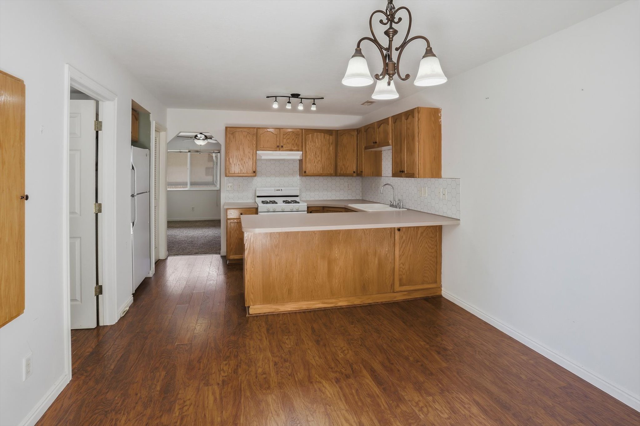 Kitchen area featuring wood-finish flooring, light wood cabinetry, white appliances, and a peninsula countertop