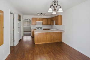 Kitchen area featuring wood-finish flooring, light wood cabinetry, white appliances, and a peninsula countertop