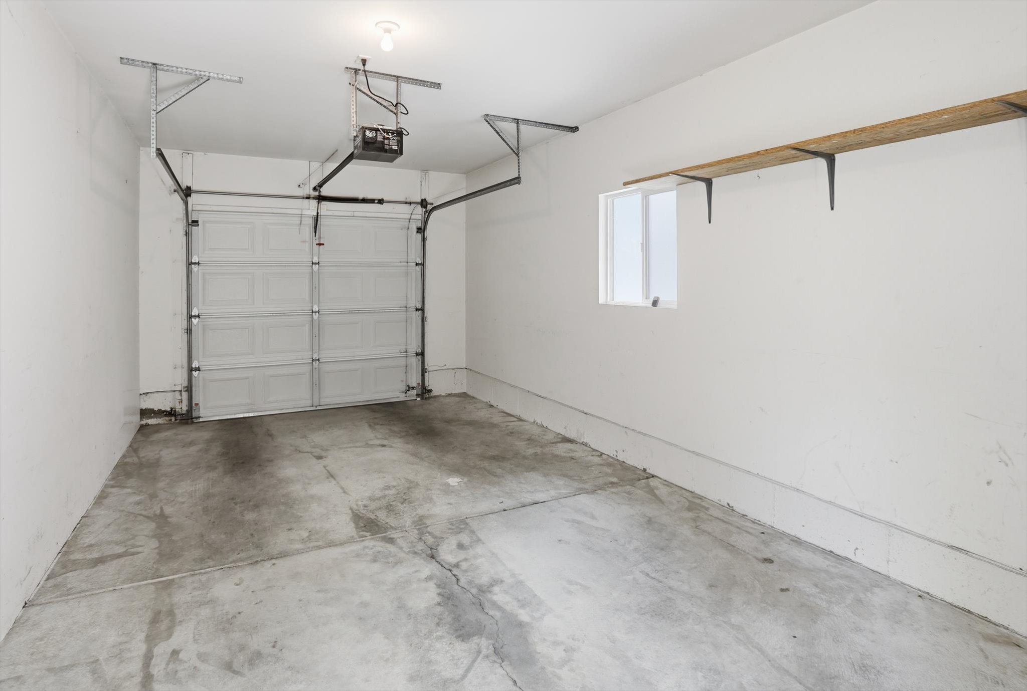 Single-vehicle garage with a panel garage door, concrete flooring, and an automatic garage door opener