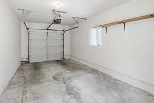 Single-vehicle garage with a panel garage door, concrete flooring, and an automatic garage door opener