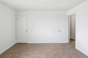Carpeted room featuring two white paneled doors with gold-toned hardware, white baseboards, and a neutral ceiling