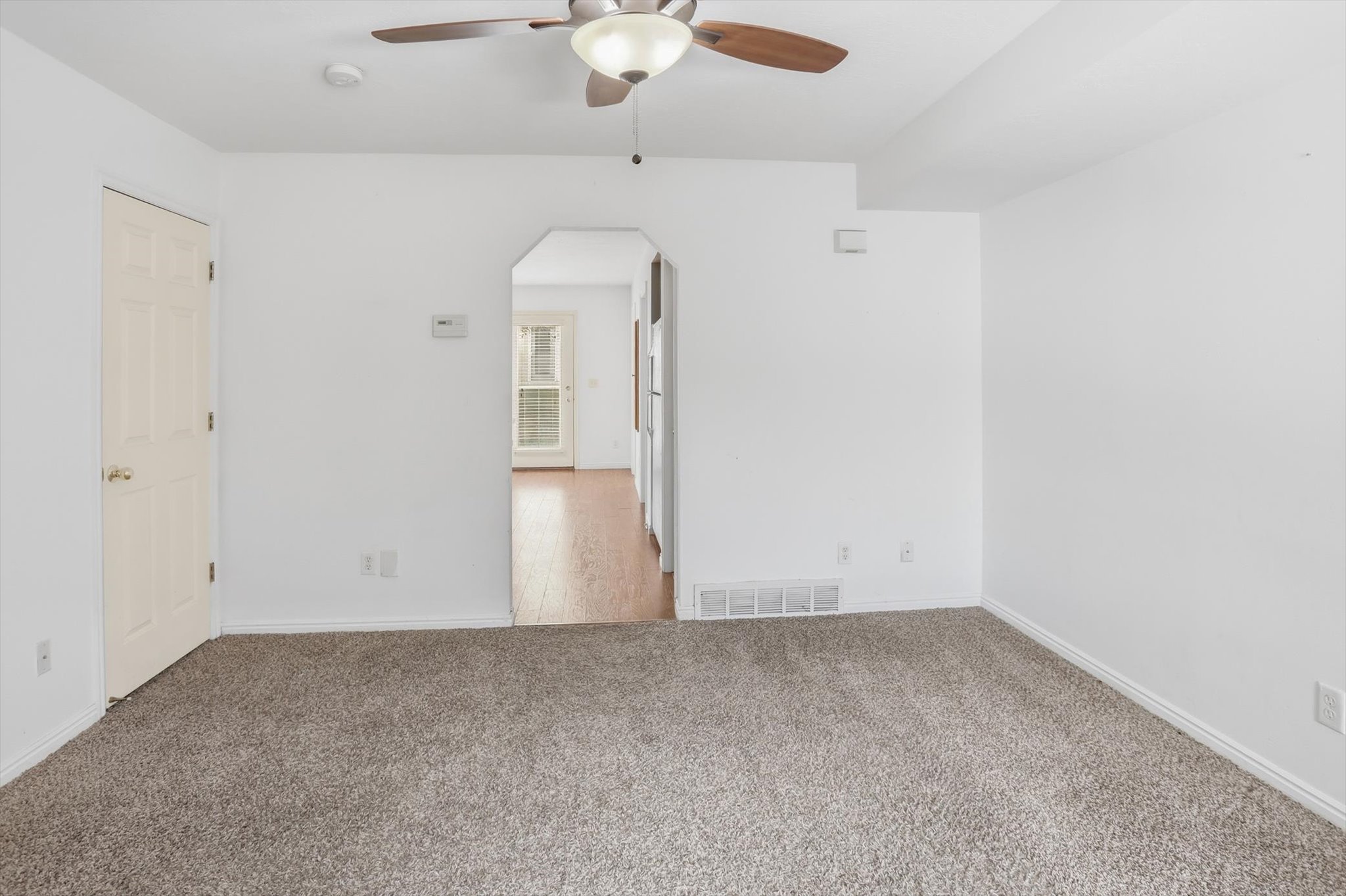 Carpeted living area with white walls and a ceiling fan