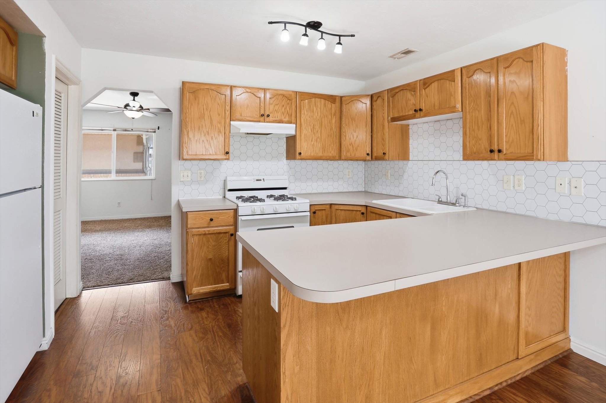 Kitchen featuring wood-finish flooring, light wood cabinetry, white hexagonal tile backsplash, a white gas range, and a breakfast bar with a light-toned countertop