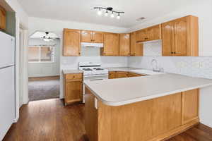 Kitchen featuring wood-finish flooring, light wood cabinetry, white hexagonal tile backsplash, a white gas range, and a breakfast bar with a light-toned countertop
