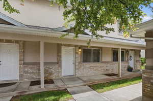 Exterior facade featuring a covered patio, brick detailing, stucco siding, multiple entry doors, and wall-mounted lighting fixtures