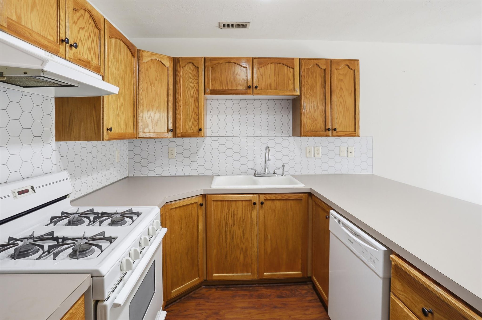 Kitchen featuring wood cabinetry, hexagon tile backsplash, durable countertops, and a white gas range with a matching range hood