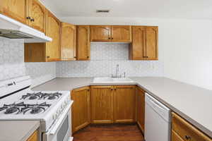 Kitchen featuring wood cabinetry, hexagon tile backsplash, durable countertops, and a white gas range with a matching range hood