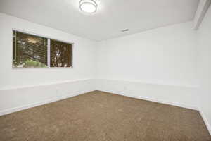 Front downstairs bedroom with neutral-toned carpeting complements bright white walls in this room, featuring a window with horizontal blinds and a flush-mount ceiling light fixture