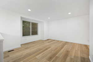 Bright interior space featuring a window with exterior tree scenery, wood-finish flooring, recessed lighting, white baseboards, and crisp white walls