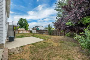 Spacious backyard with a large concrete patio, mature trees, and a newly built Trex deck with metal railings