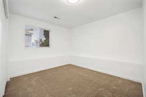 Back downstairs bedroom with neutral-toned carpeted room featuring white walls and a large window with horizontal blinds, double wide closet with bi-fold doors