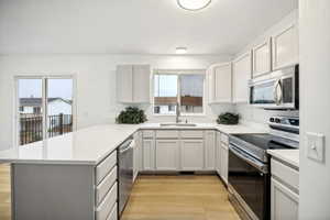 U-shaped kitchen featuring tan cabinetry, light countertops, wood-finish flooring, stainless steel appliances, and a sliding glass door