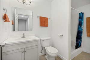 Bathroom featuring a tan vanity with an integrated sink, polished chrome faucet, square mirror, and a full-sized toilet
