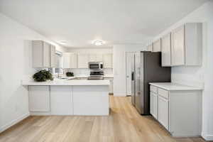 Modern kitchen featuring light wood-finish flooring, tan cabinetry, integrated stainless steel appliances, and quartz countertops