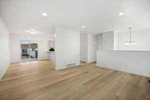 Spacious open-concept living area featuring light wood-finish flooring, recessed lighting, and a modern chandelier