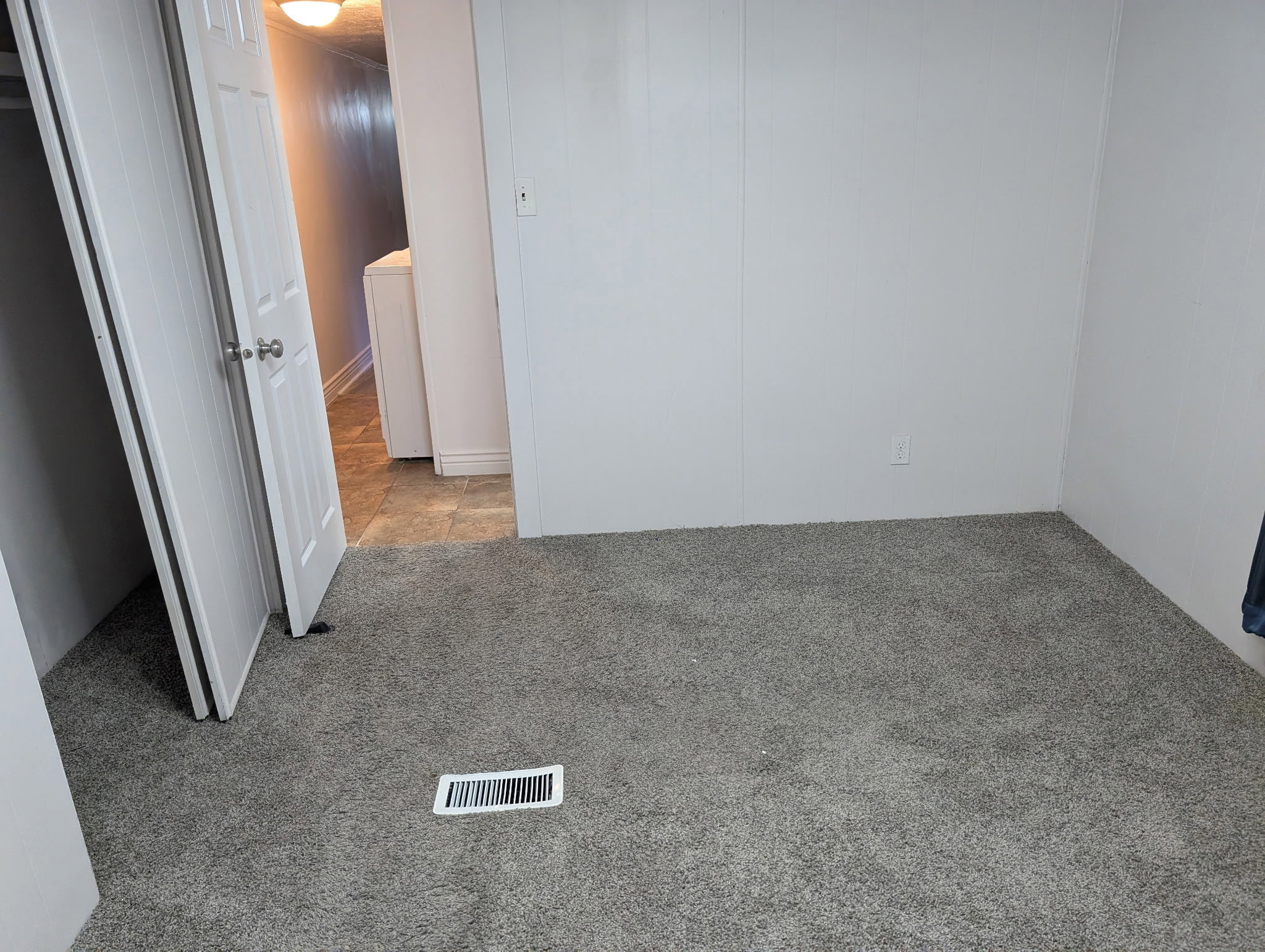 Grey carpeted room with white paneled walls and a white interior door