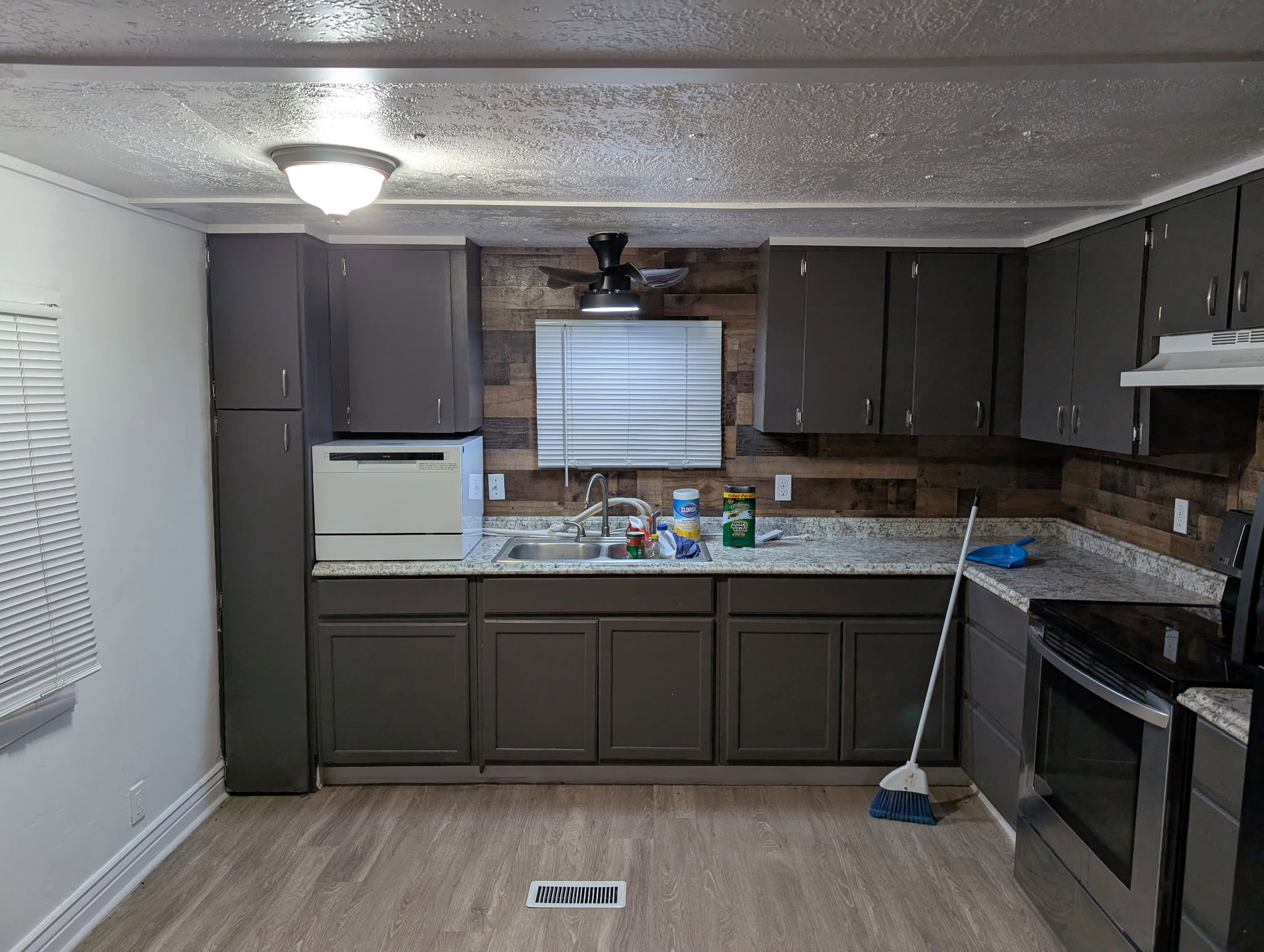 Kitchen featuring wood-finish flooring, dark gray cabinetry, light speckled countertops, a wood plank accent wall, and a stainless steel oven