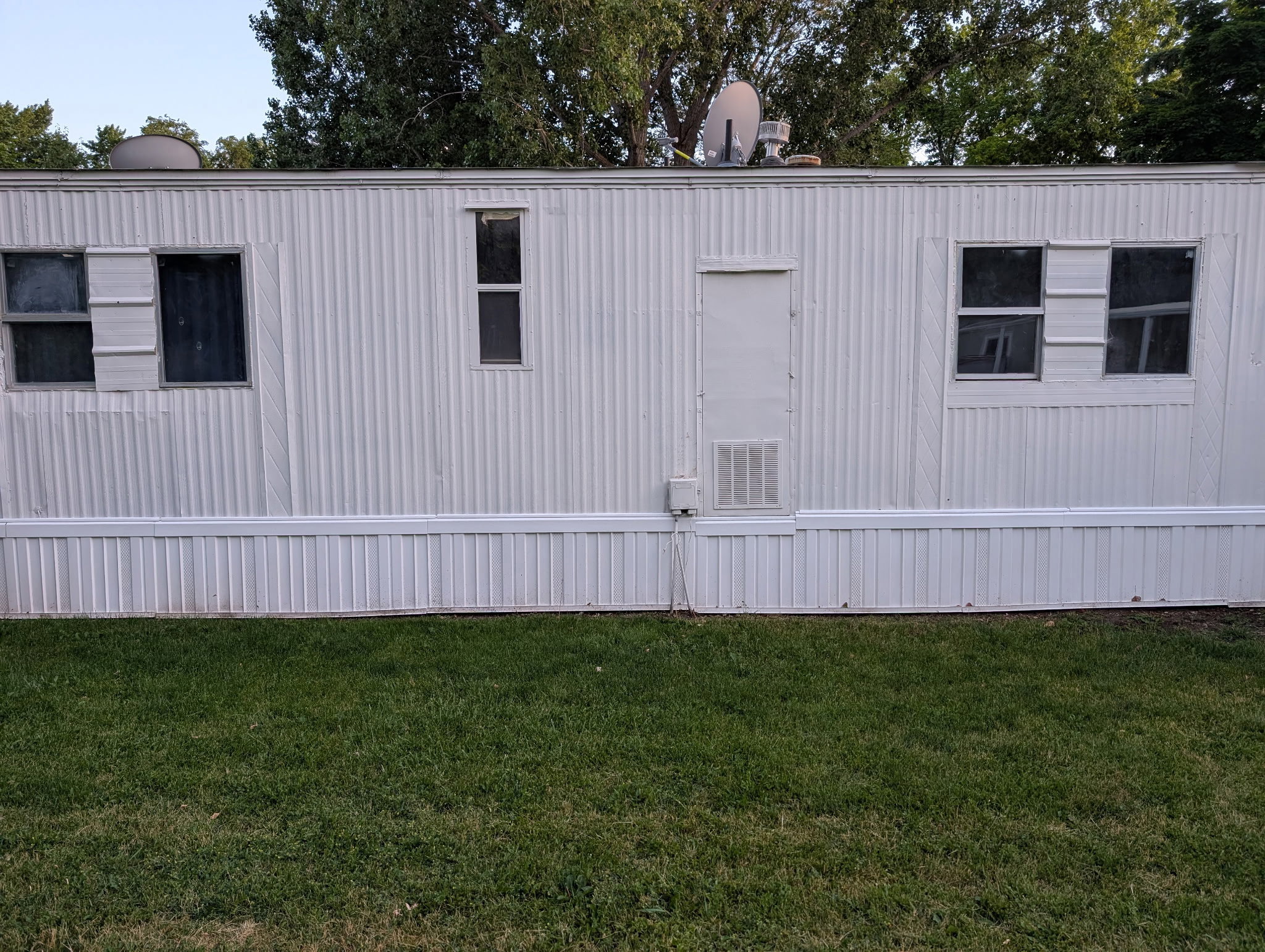 White corrugated siding exterior with multiple windows, a side entry door, and a green lawn foreground