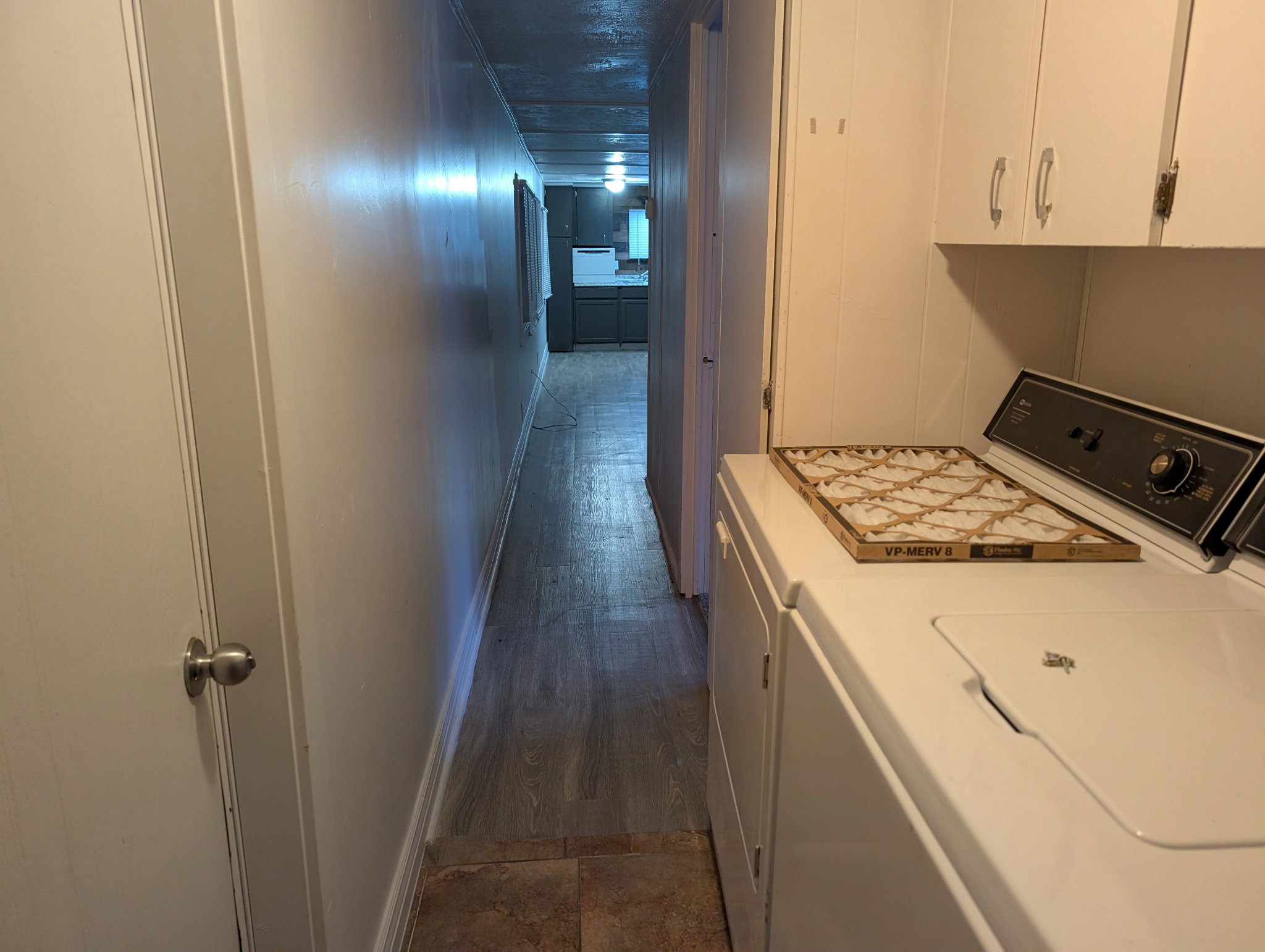 Laundry area featuring white cabinetry, light-toned wall paneling, and a tile-finish floor