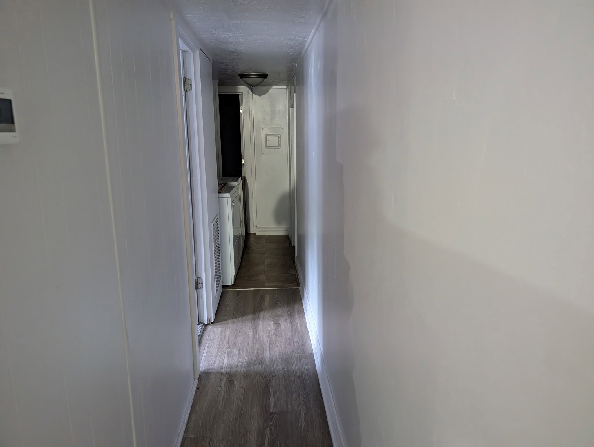 Hallway featuring wood-finish flooring, white paneling, and a flush-mount ceiling light