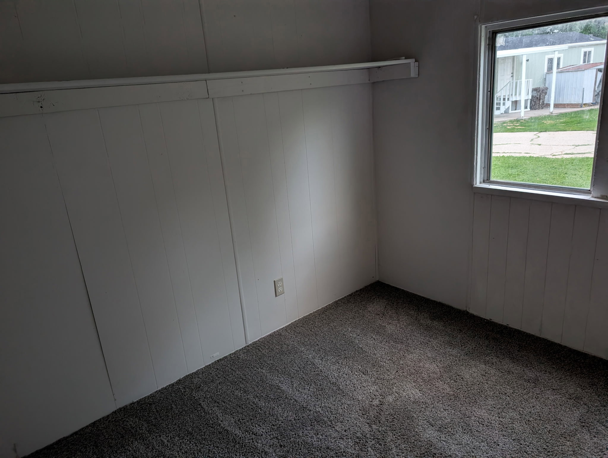 Room featuring dark gray carpet flooring, white paneled walls, and a white-framed window